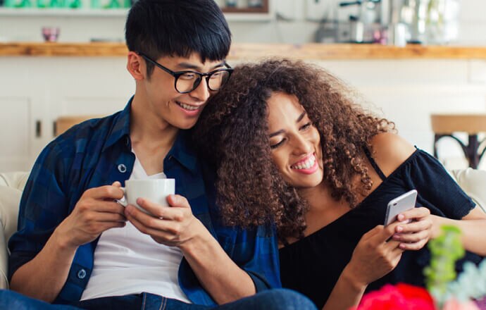 man en vrouw op bank kijken naar een mobiele telefoon met beschermd van Norton 360 for Mobile.