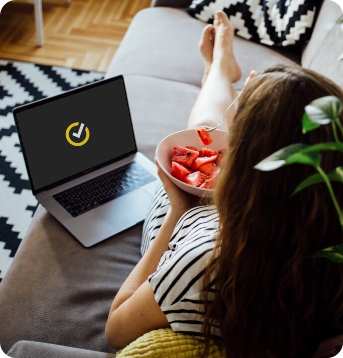 Vrouw die fruit eet met laptop naast haar waarop het symbool van NortonLifeLock is te zien.
