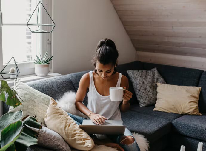 Vrouw met een mok zit op de bank met een laptop