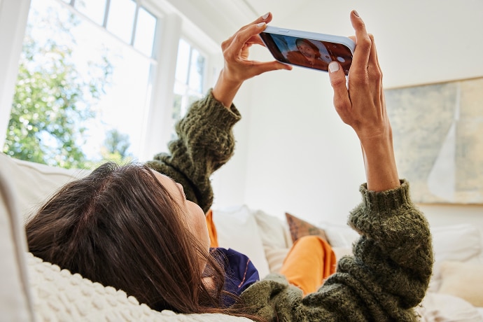Liggende vrouw die naar een mobiele telefoon kijkt